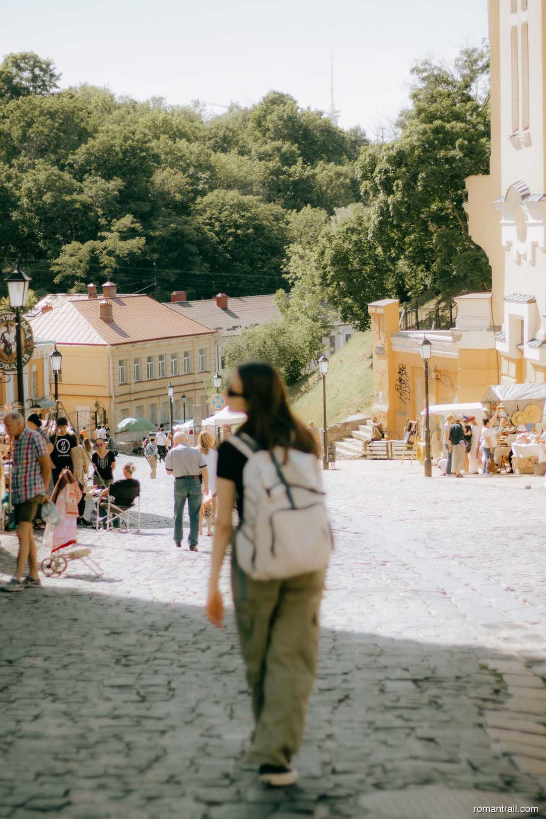 Woman walking a cobblestone city street wearing a white travel daypack