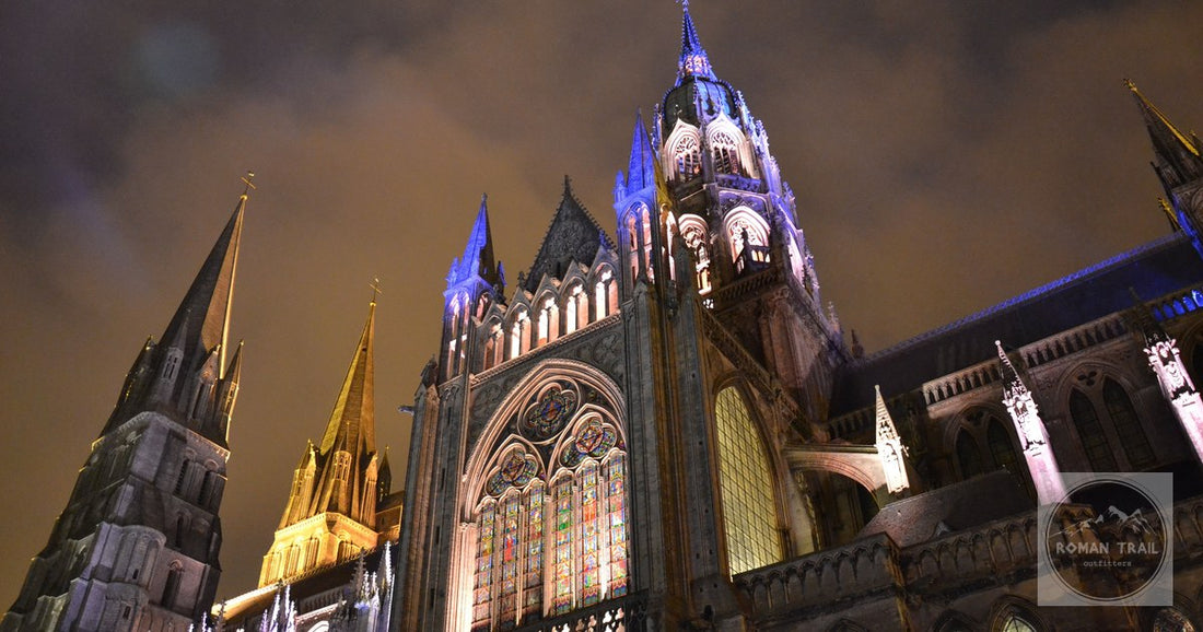 Dramatic night view of Bayeux Cathedral illuminated with colorful lights.
