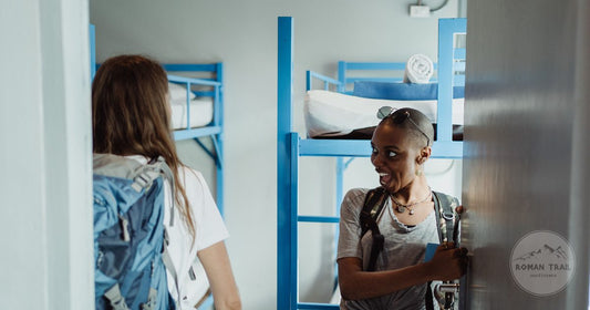 Two women with backpacks arriving in a hostel dormitory
