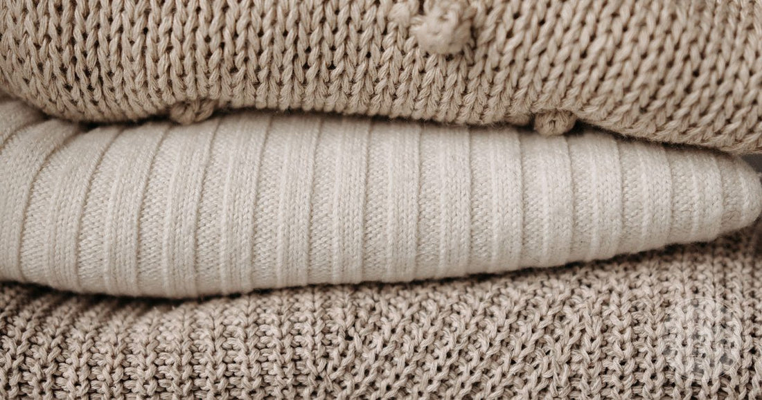 A stack of folded beige knitted garments showing different knit patterns