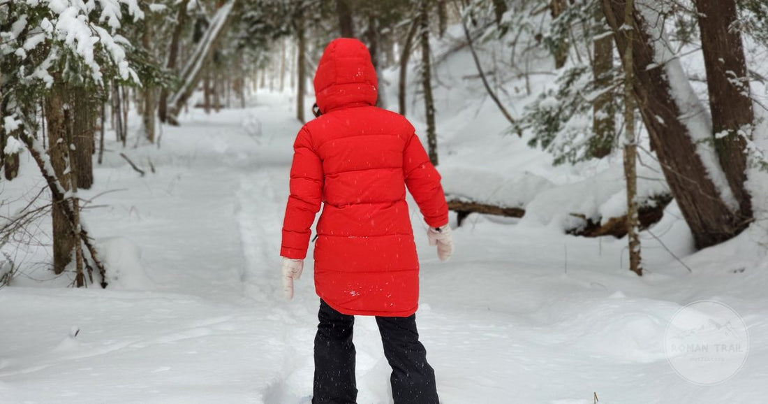 A person in a red coat snowshoeing through a snow covered forest