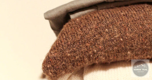 Folded warm-toned wool knitwear close-up, merino wool vs cotton for travel by Roman Trail Outfitters