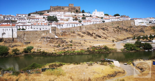 Picturesque Mértola town with its iconic castle and river Grande under a clear blue sky.