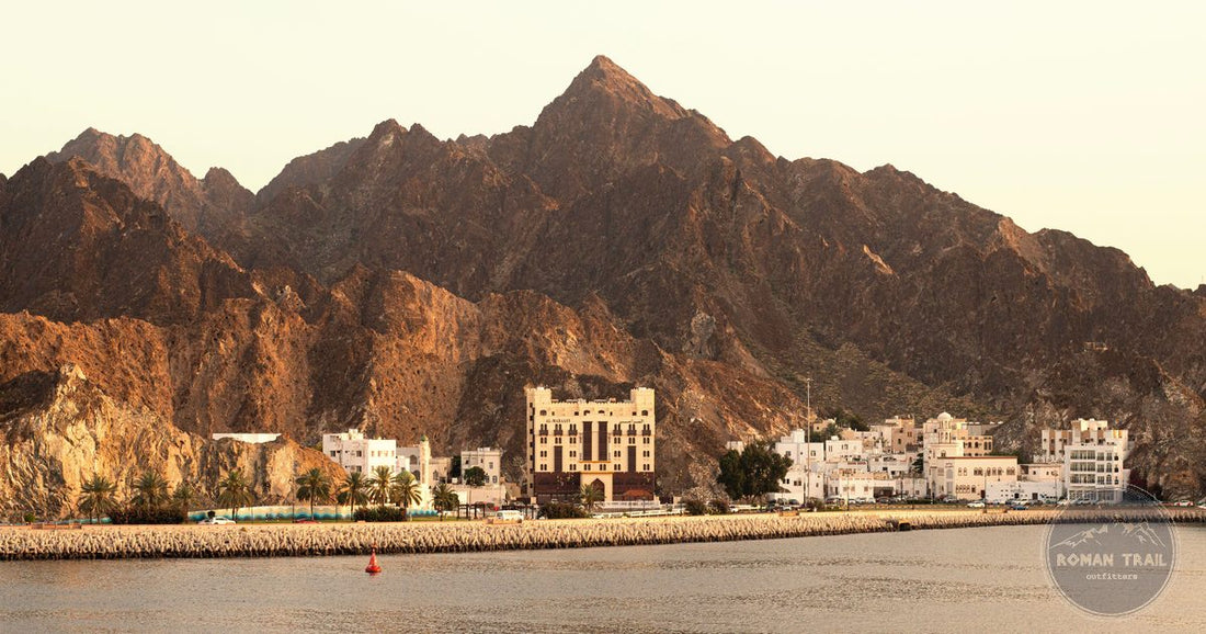 Mutrah harbor and traditional buildings beneath rugged mountains at sunset, Muscat, Oman