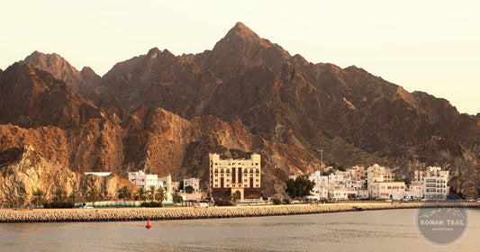 Mutrah harbor and traditional buildings beneath rugged mountains at sunset, Muscat, Oman