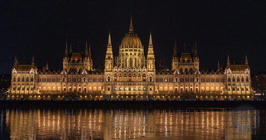 Hungarian Parliament building illuminated and reflected in the Danube River at night, women's Budapest packing list by Roman Trail Outfitters