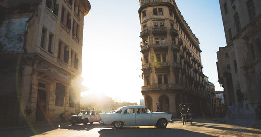 Vintage car on a Havana street at golden hour with sun flare through colonial buildings, women's Cuba packing list by Roman Trail Outfitters