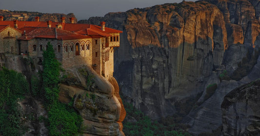 Great Meteoron Monastery in Meteora, Greece perched on a rock pillar glowing warm gold at sunset, women's travel destination