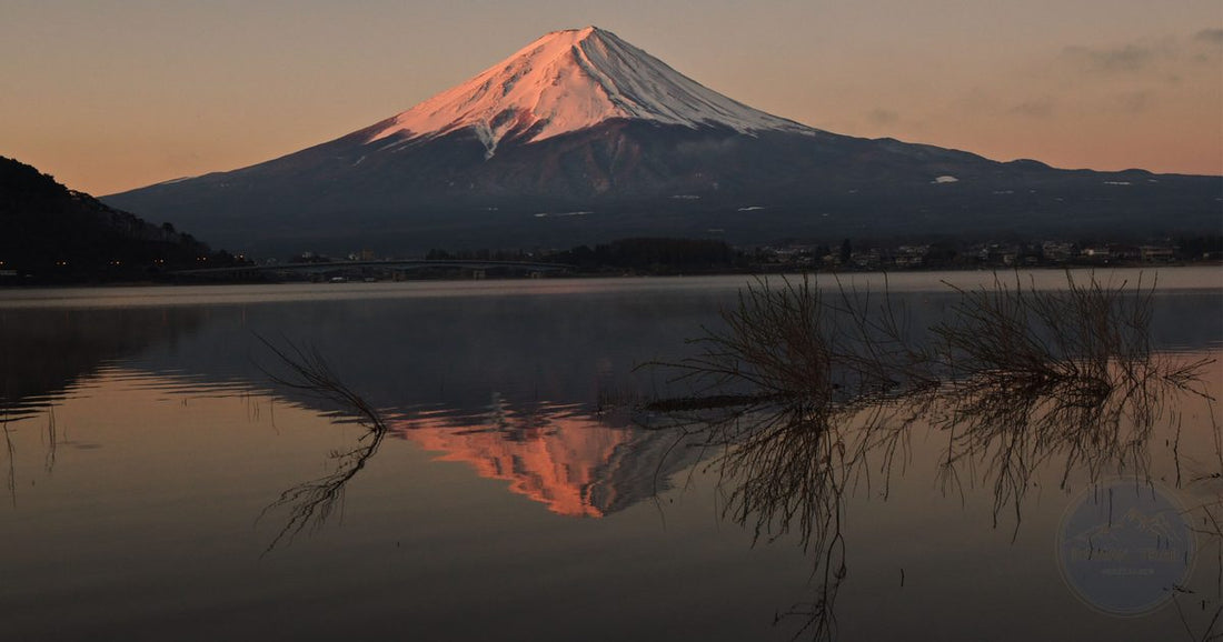 Mount Fuji at sunrise reflected in a calm lake with warm pink and orange sky, women's travel destination