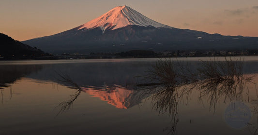 Mount Fuji at sunrise reflected in a calm lake with warm pink and orange sky, women's travel destination