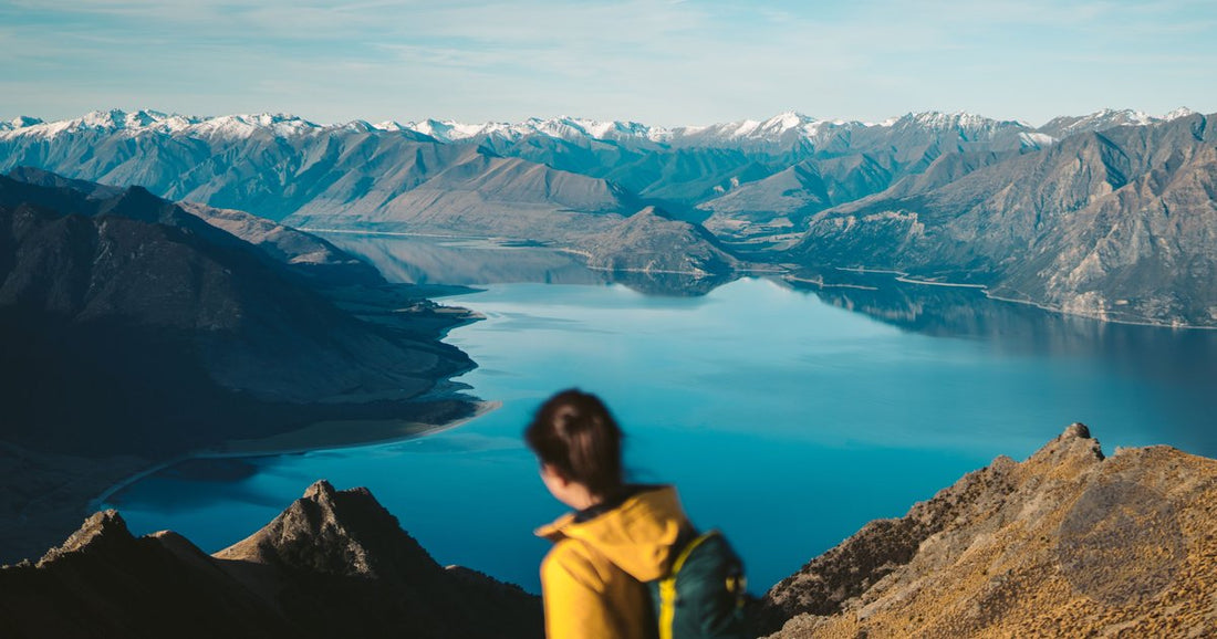 Woman hiking with backpack overlooking snow-capped Southern Alps and alpine lake in Otago New Zealand - Roman Trail Outfitters New Zealand packing list
