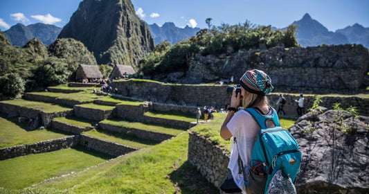 Woman hiking with backpack photographing Machu Picchu terraces and mountains in Peru - Roman Trail Outfitters Peru packing list
