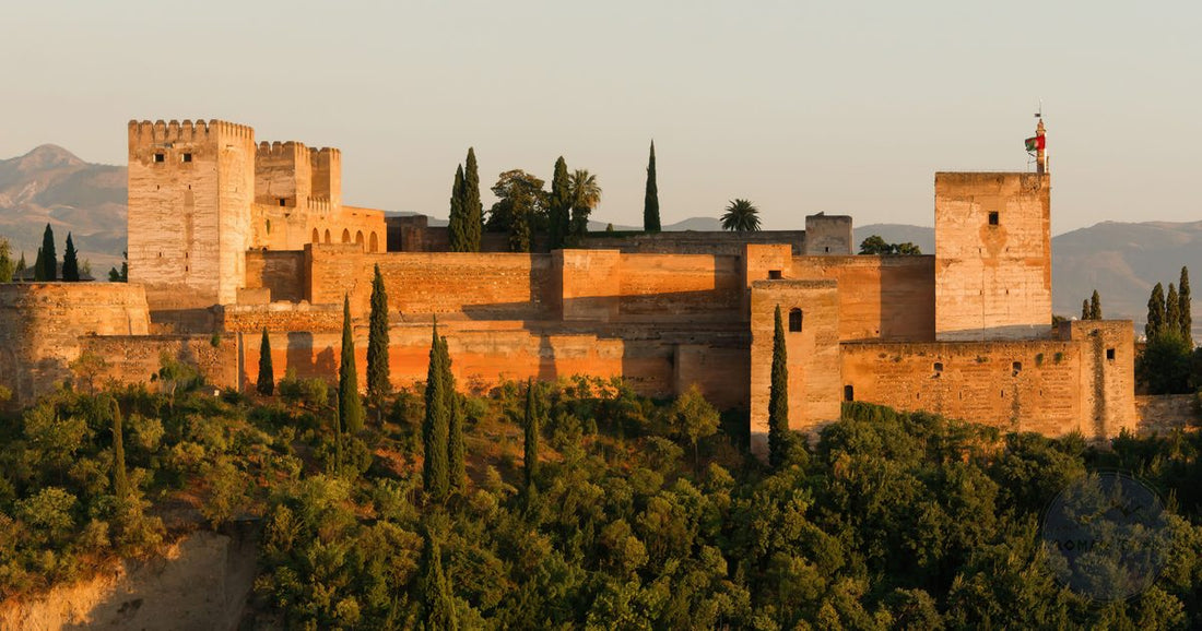 The Alhambra fortress glowing warm gold at sunset above green cypress trees in Granada, Spain - Roman Trail Outfitters Spain packing list