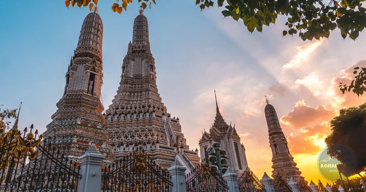 Wat Arun temple spires in Bangkok, Thailand silhouetted against a warm golden sunset sky, women's travel destination