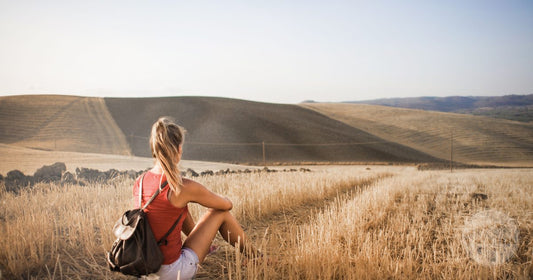 A woman with a backpack watching the sunset alone in an open field