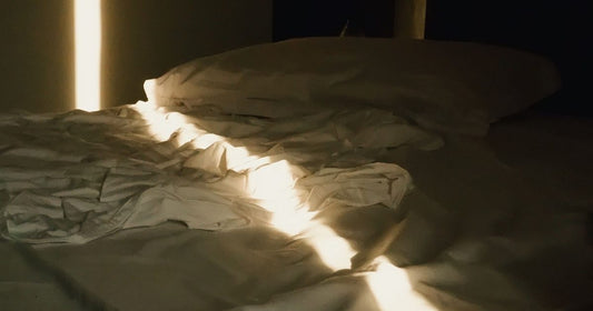 A single beam of warm morning light cutting across an unmade bed in darkness