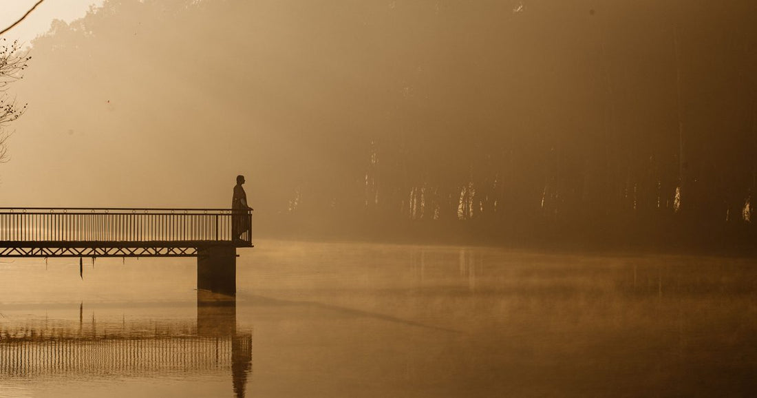 Solitary silhouette standing on a pier over misty golden water at sunrise