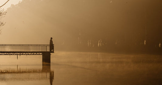 Solitary silhouette standing on a pier over misty golden water at sunrise