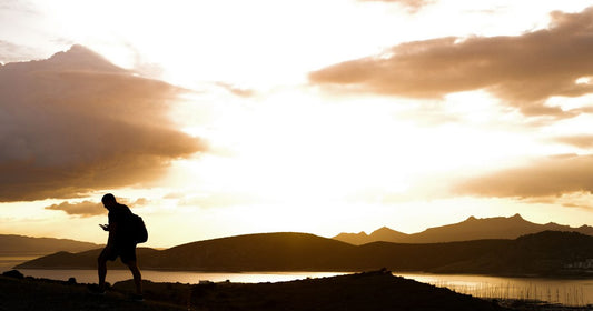 Silhouette of a lone hiker with backpack against a dramatic golden sunset sky overlooking mountains and water