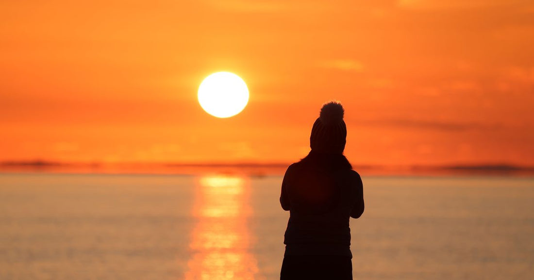 Silhouette of a woman watching the sunset over the water, contemplative and alone