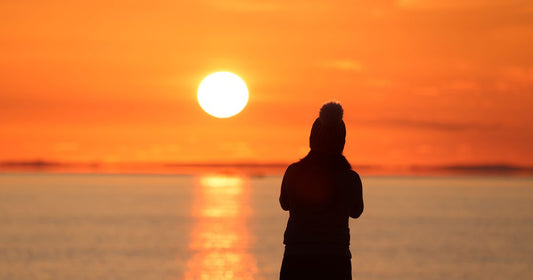 Silhouette of a woman watching the sunset over the water, contemplative and alone