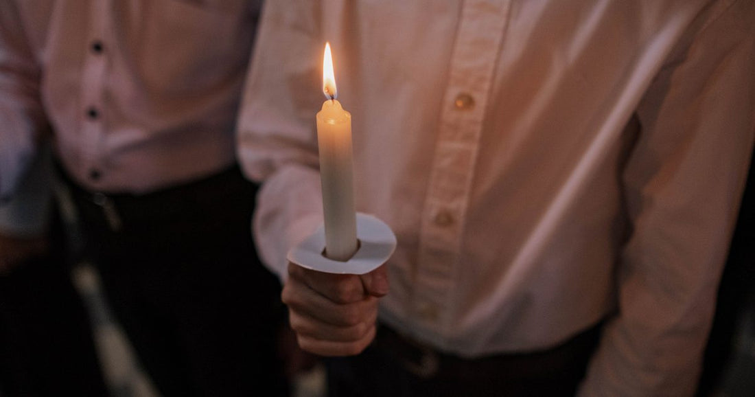 A single candle held in warm light against darkness, a quiet moment of witness and reflection