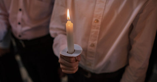 A single candle held in warm light against darkness, a quiet moment of witness and reflection