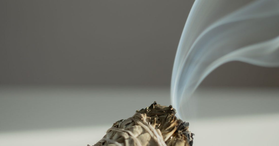 White sage smudge stick with smoke curling upward against a warm neutral background