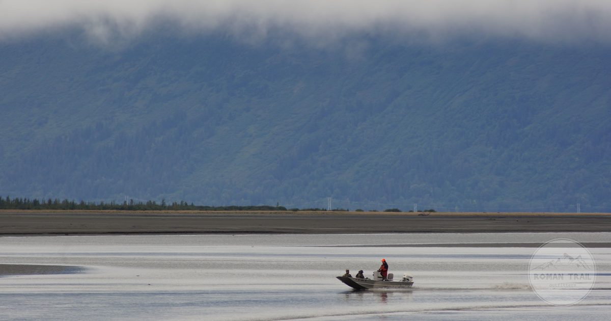Two people boating on calm water below mountains near Anchorage, Alaska