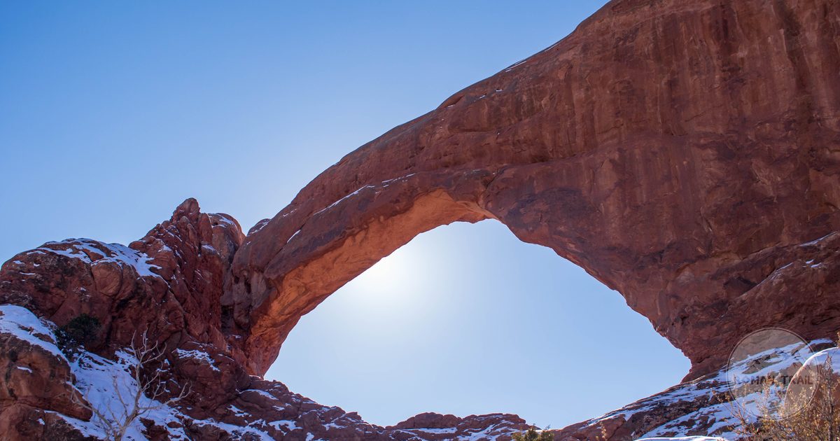 A sunlit sandstone arch with snow on the ground in Arches National Park, Utah