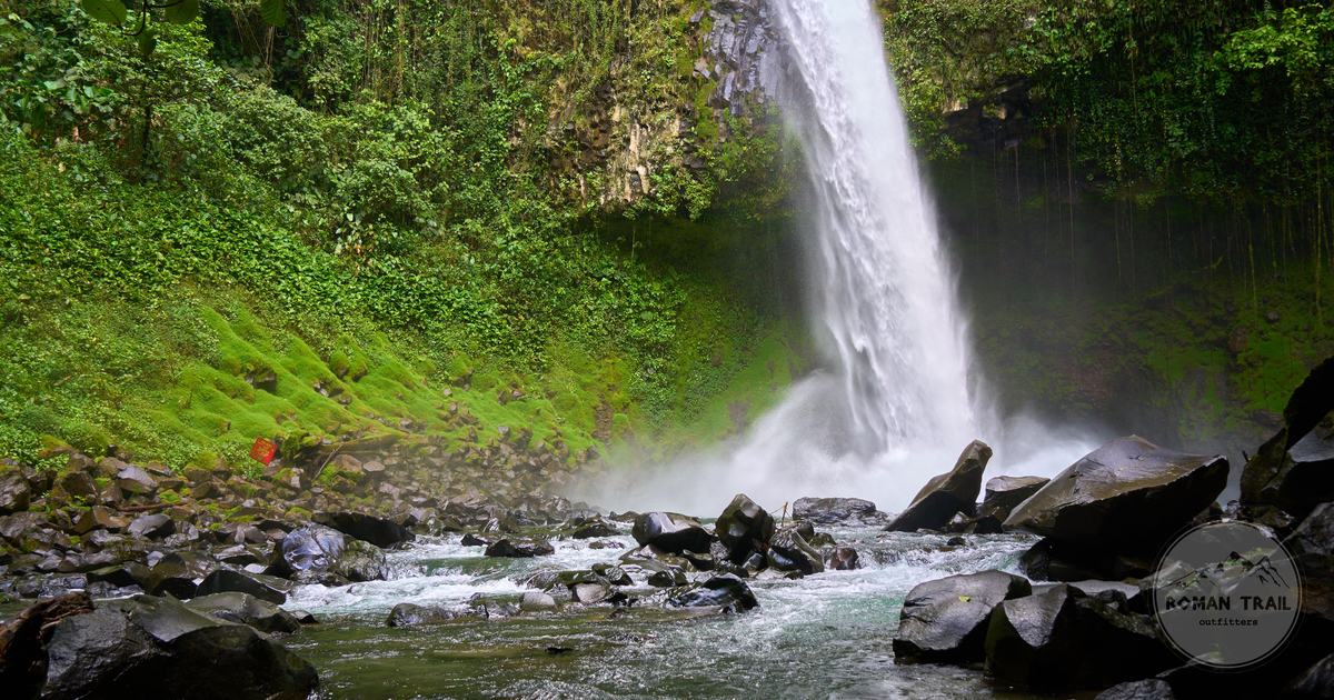La Fortuna waterfall falling into a green pool surrounded by rainforest, Arenal packing list for women by Roman Trail Outfitters