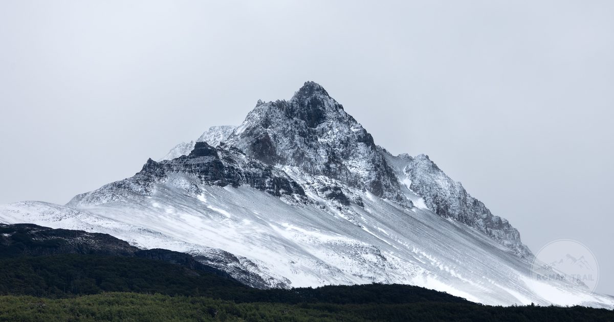 A snowy mountain peak above dense forest under winter cloud