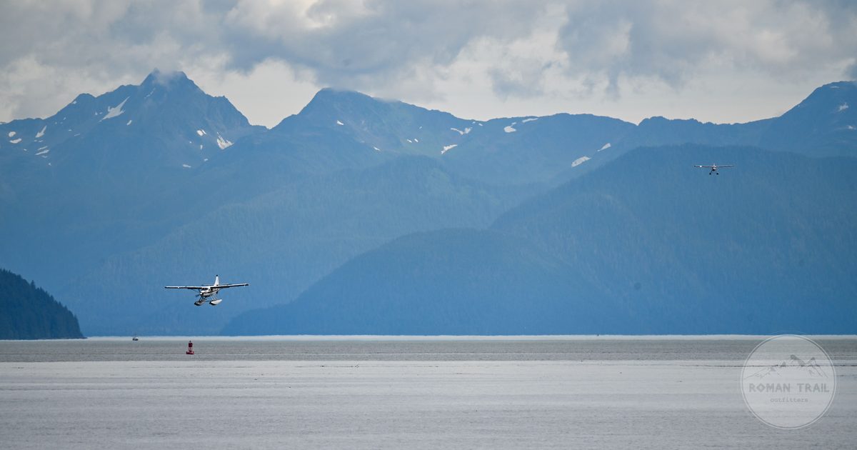 A seaplane landing at Juneau, Alaska, below mountains and cloud