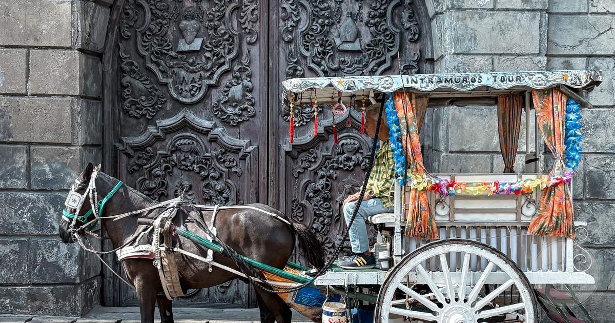 A horse-drawn carriage parked before an ornate stone gate in Manila, Philippines