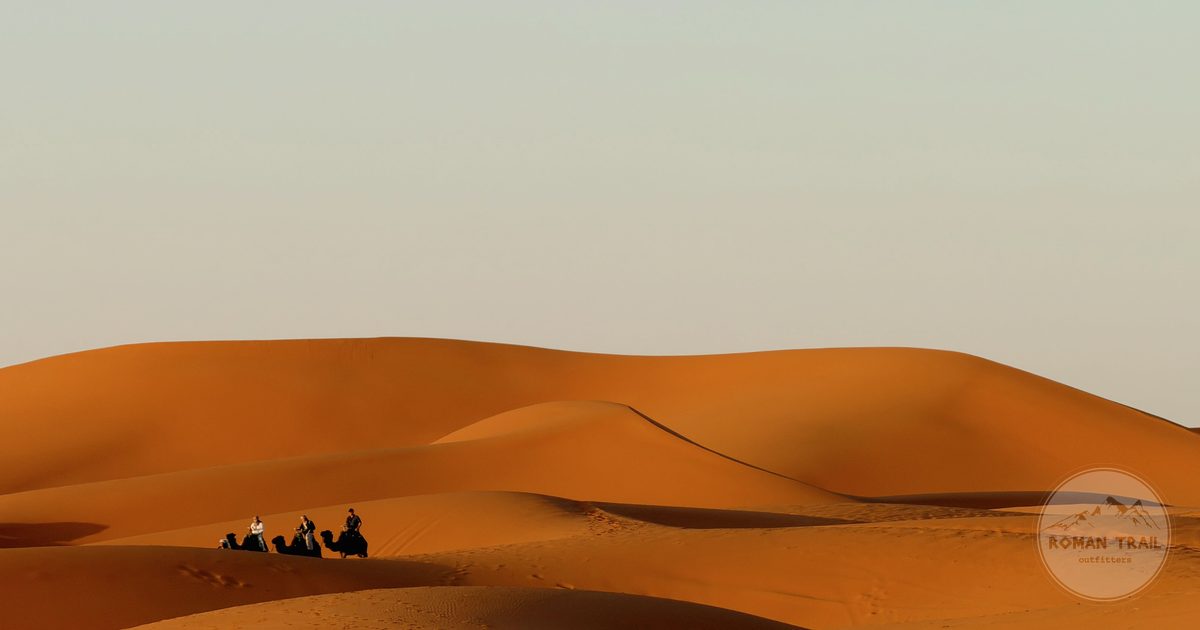 A camel train crossing the rolling Sahara dunes near Merzouga, Merzouga packing list for women by Roman Trail Outfitters