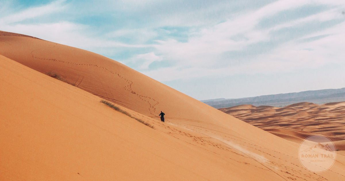 A lone walker crossing the vast sand dunes at Merzouga, Merzouga packing list for women by Roman Trail Outfitters