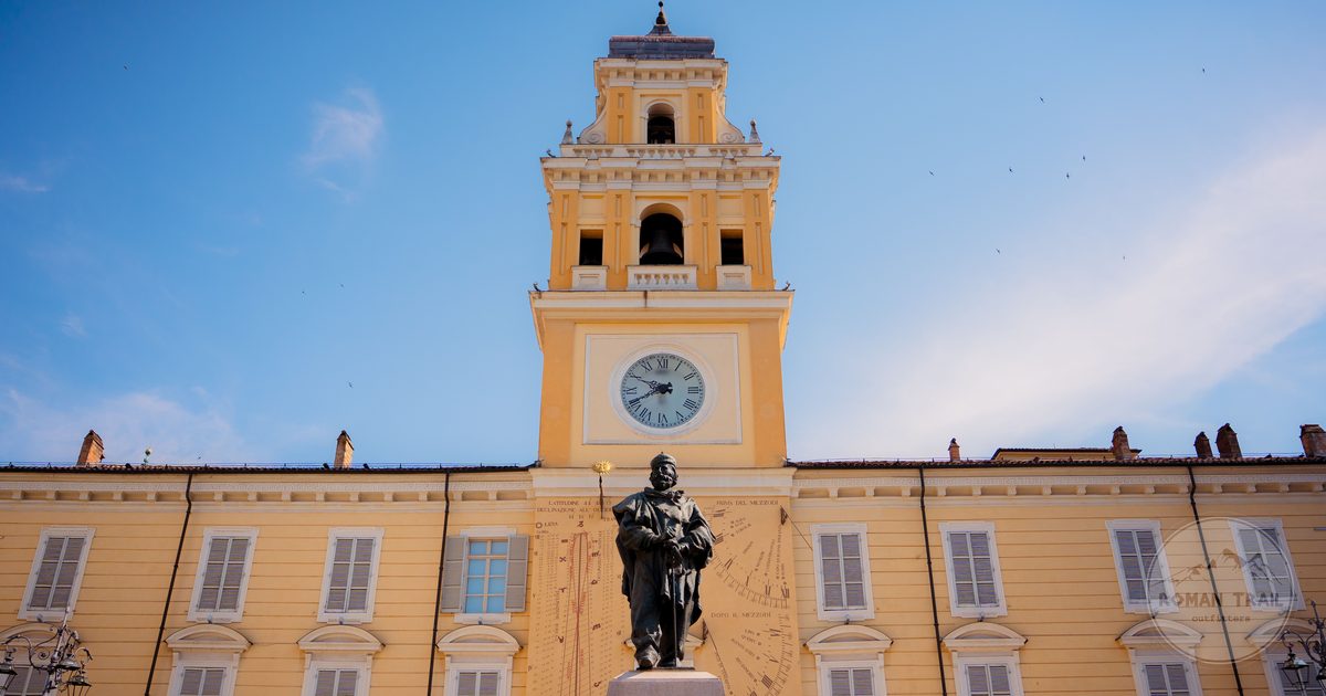 A historic clock tower and statue under clear sky in Parma, Italy
