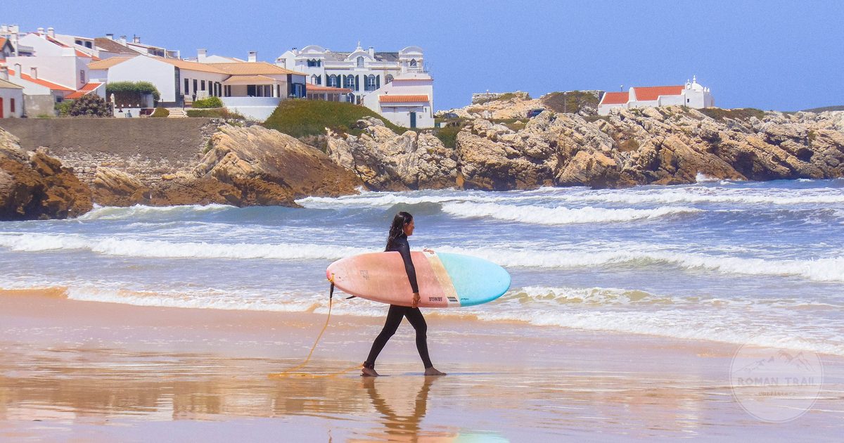 A surfer carrying a board along the beach at Peniche, Portugal