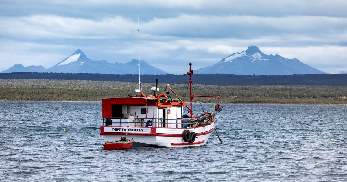 A wooden fishing boat on calm water below mountains at Puerto Natales, Chile