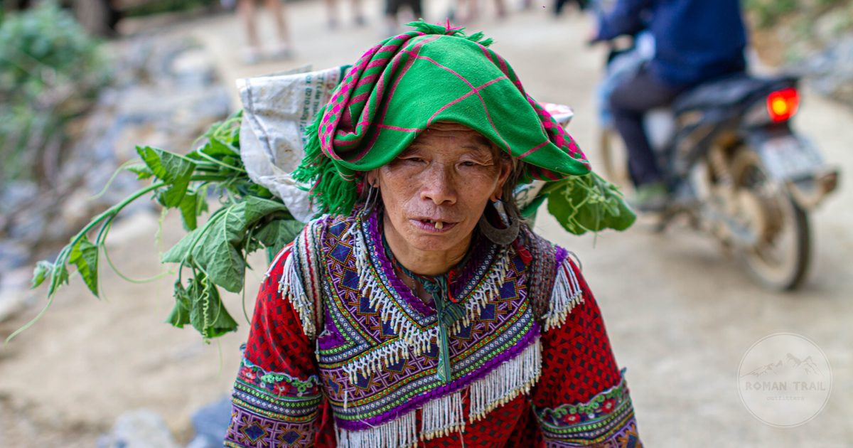 A Hmong woman in traditional indigo dress carrying greens in Lao Cai, Vietnam