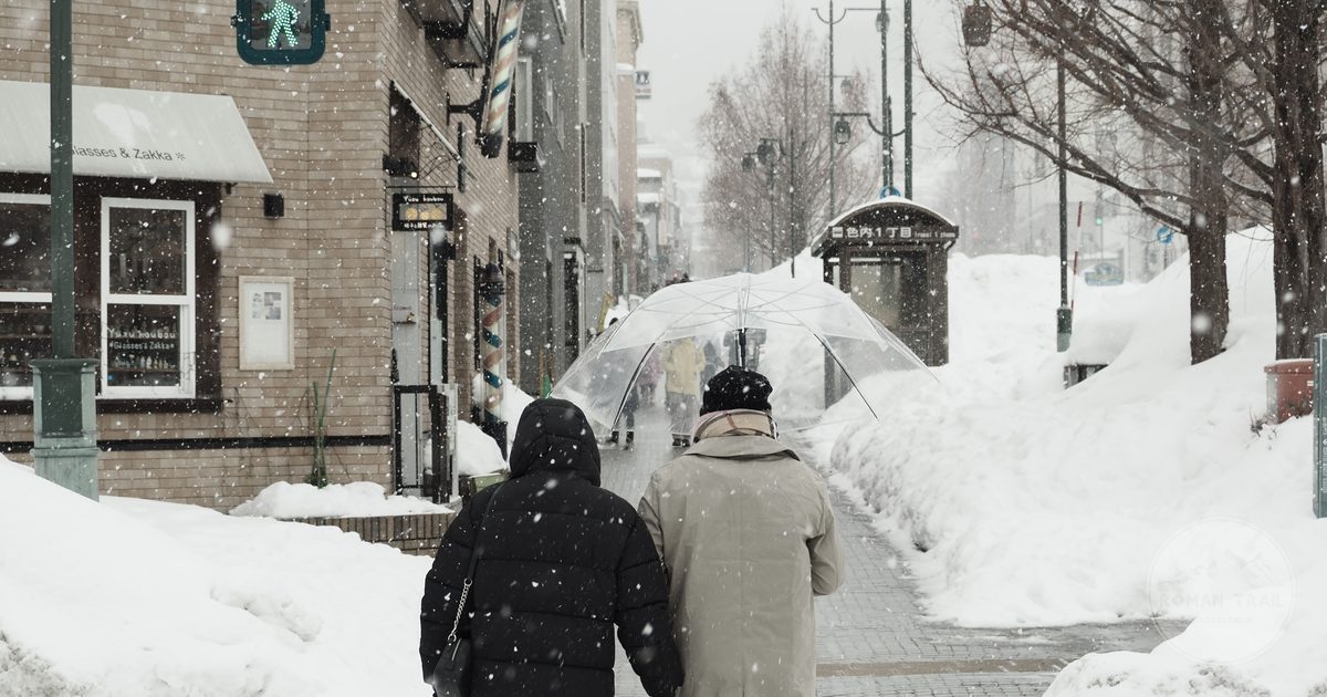 A snow covered Sapporo street with people walking in winter, Sapporo packing list for women by Roman Trail Outfitters