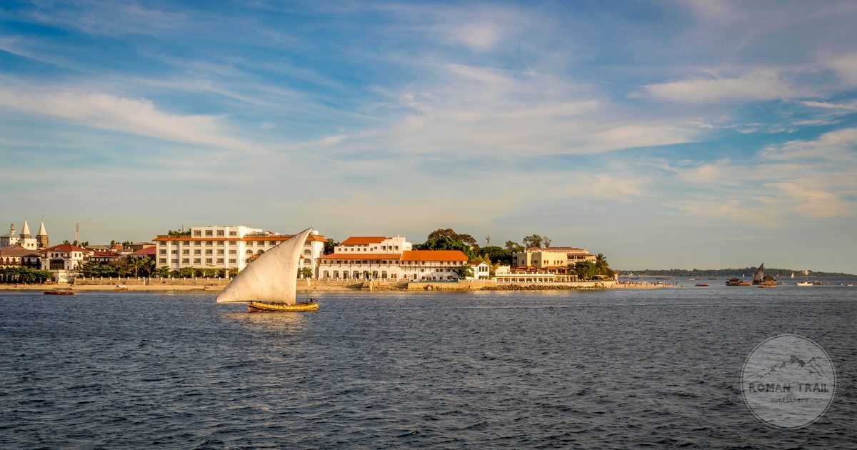 A sailing dhow on the water before the Stone Town skyline, Zanzibar